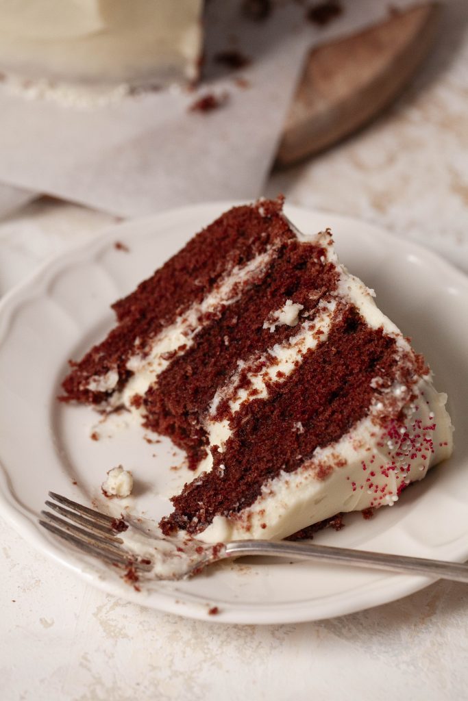 a piece of red velvet cake on a plate with a bite taken out of it. 